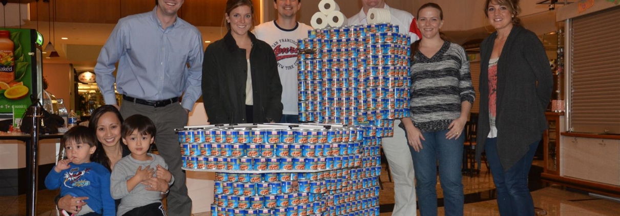 Image of a group of members from Jordan & Skala Engineers standing around a giant toilet made from individual cans to represent the canstruction competition to help distribute cans to Atlanta food banks.