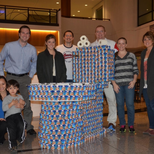 Image of a group of members from Jordan & Skala Engineers standing around a giant toilet made from individual cans to represent the canstruction competition to help distribute cans to Atlanta food banks.